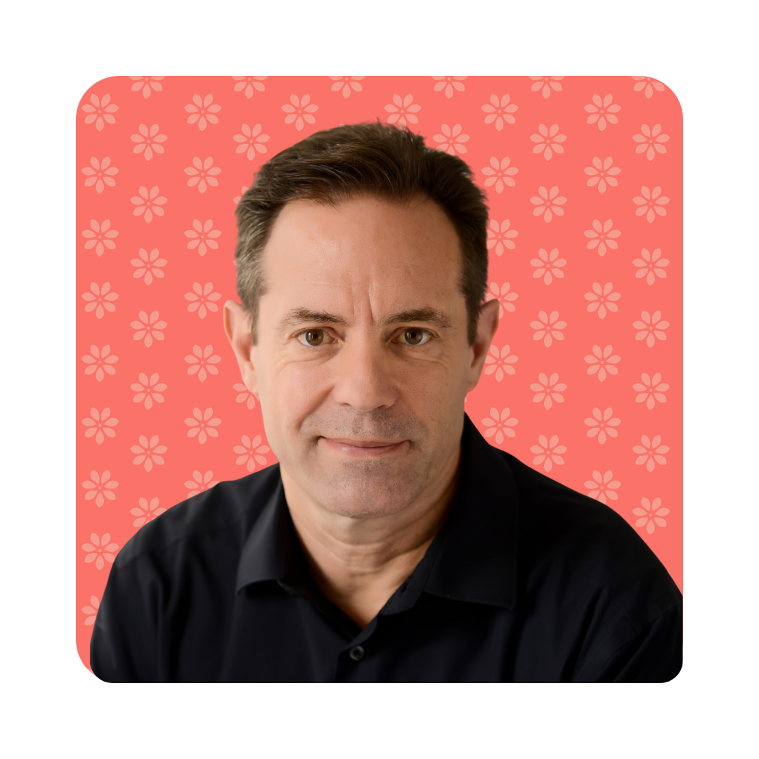therapist (2) Portrait of a smiling therapist at Total Life with light skin and short dark brown hair, wearing a black collared shirt. The background features a soft coral color with a subtle floral pattern.